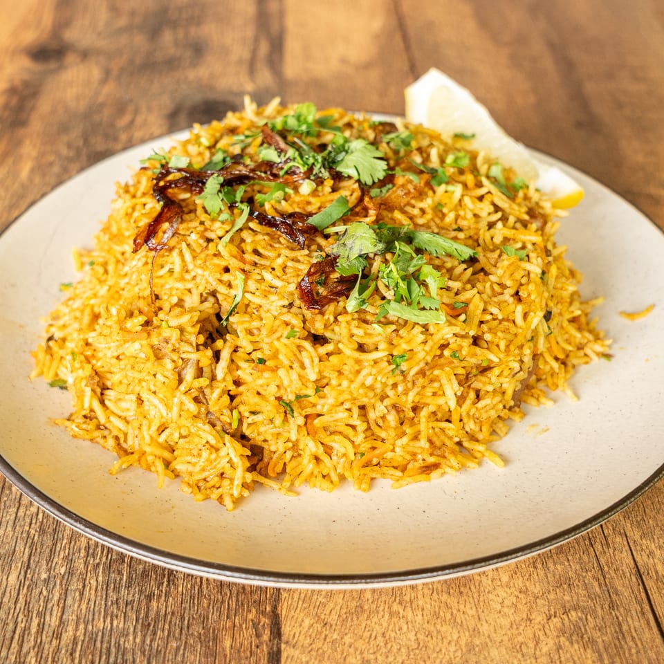 Spiced biryani rice garnished with cilantro and fried onions, served on a ceramic plate with lemon wedges.