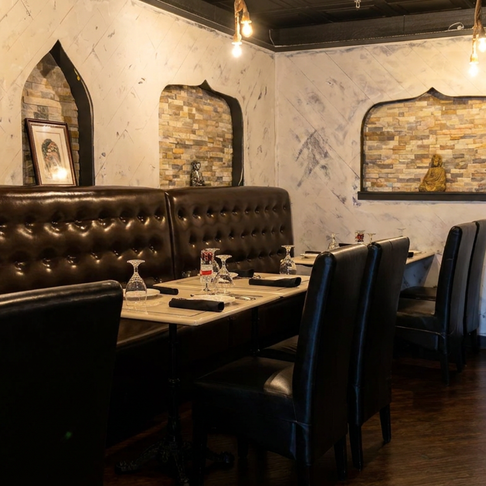 Warmly lit restaurant dining room with dark leather booths, set tables, stone alcoves, and decorative statues.