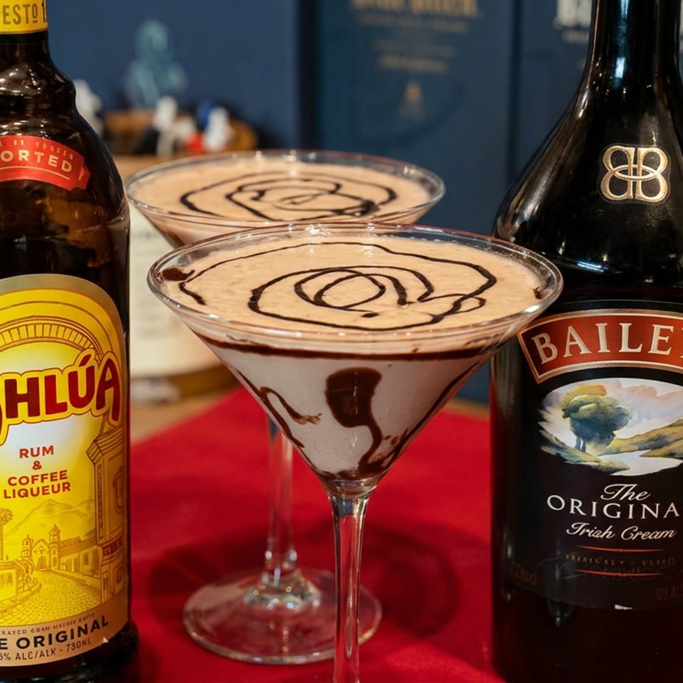 Two creamy chocolate martinis sit between Kahlúa and Baileys bottles on a red bar counter.
