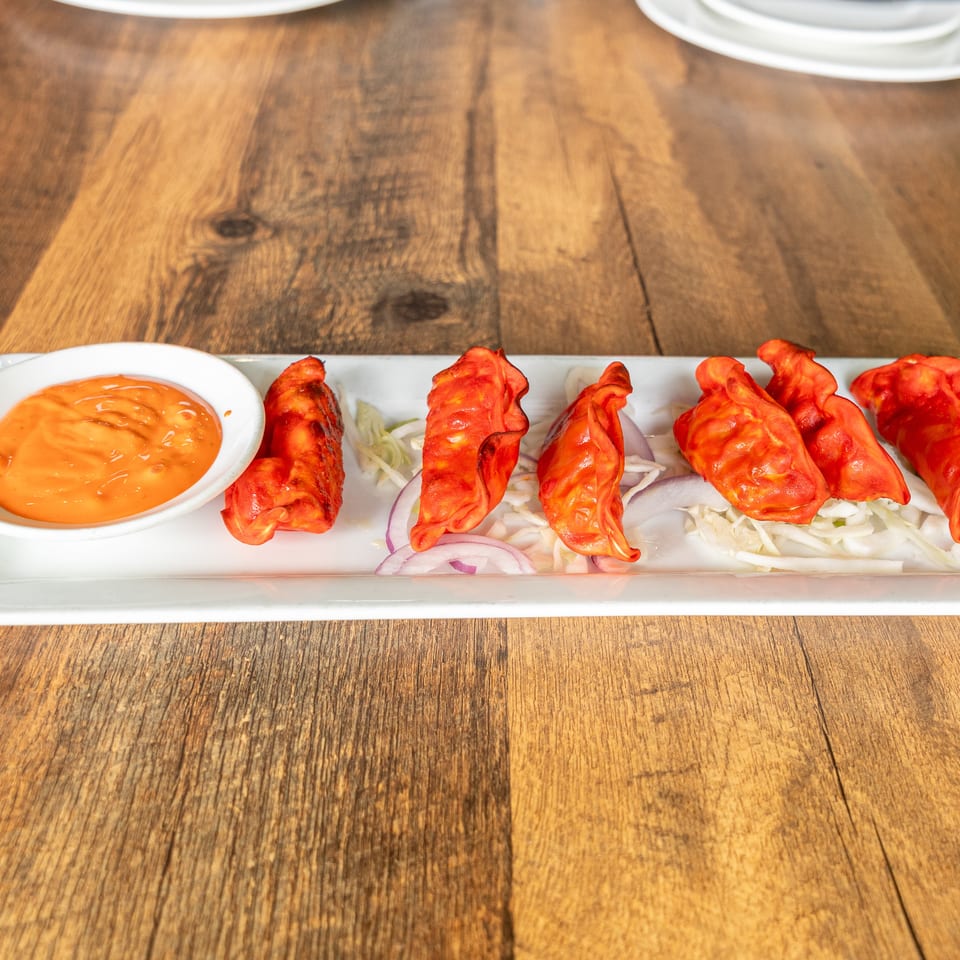 Red dumplings served with sliced onions, cabbage, and orange dipping sauce on a white platter atop a wooden table.