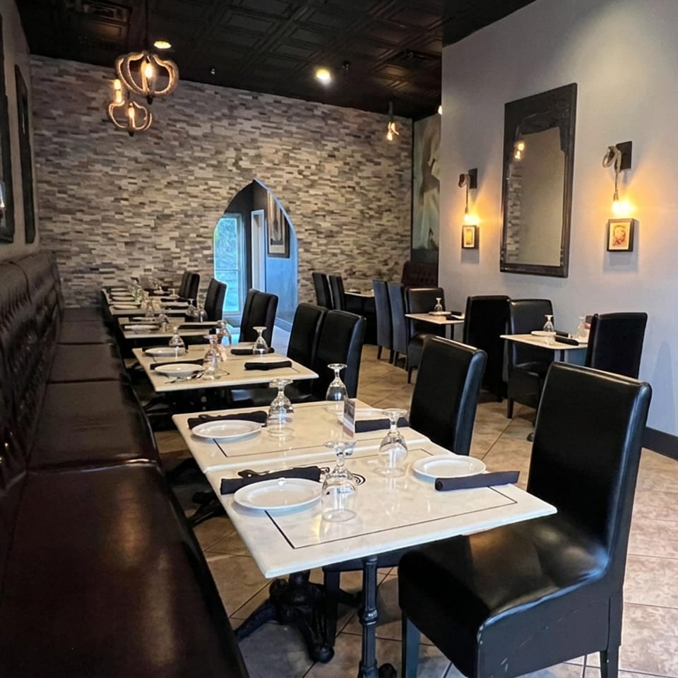 Elegant restaurant dining room with black leather seating, set tables, stone accent wall, and warm pendant lighting.
